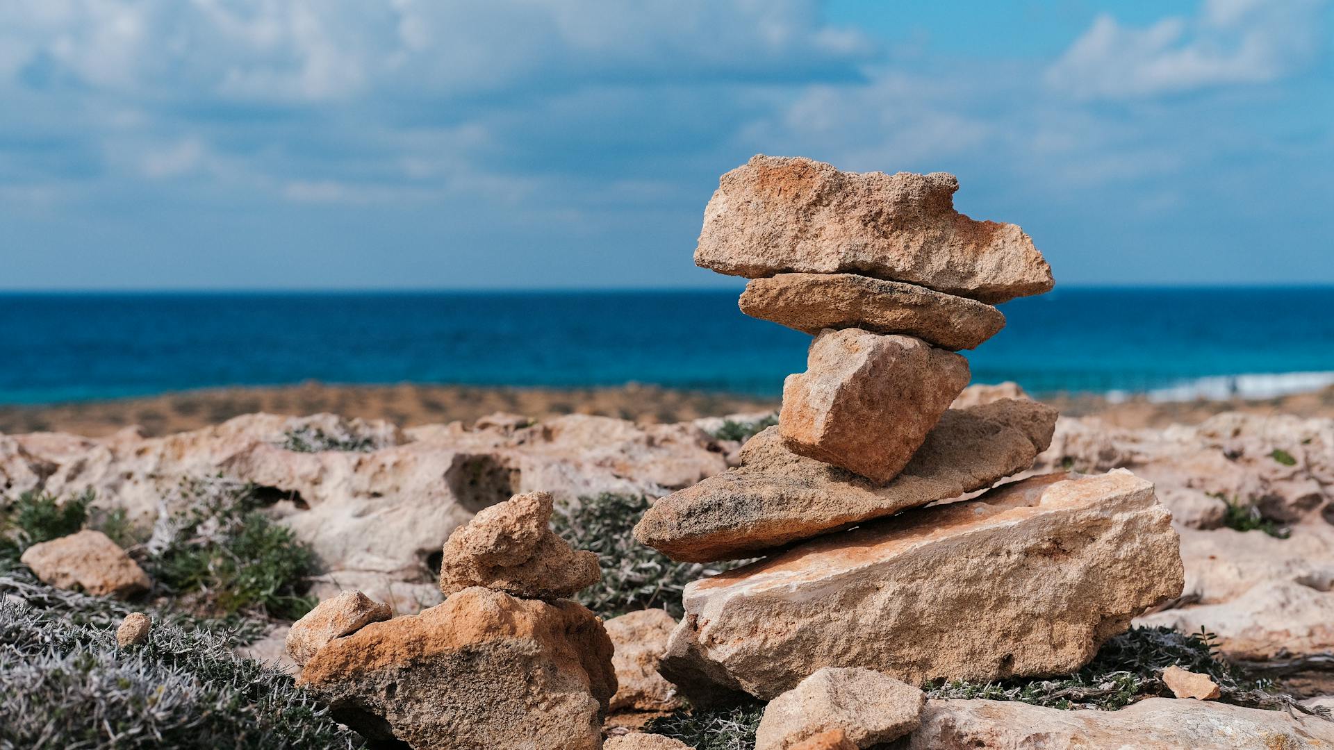 Serene view of balanced stones on rocky coast with blue sea and sky in Cyprus.