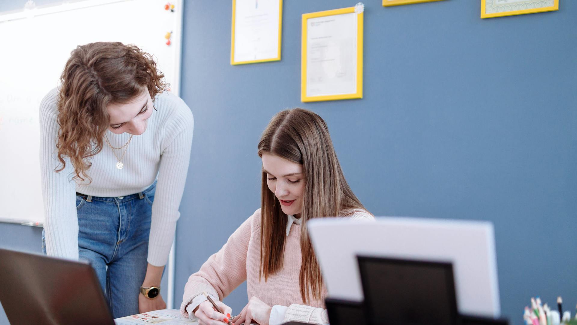 Two women working together on educational materials in a classroom setting.